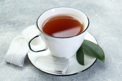 Photo of Aromatic tea in cup, teabags and green leaves on grey table