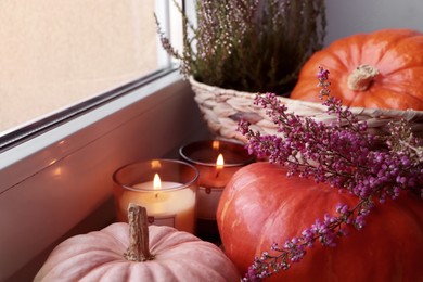 Wicker basket with beautiful heather flowers, pumpkins and burning candles near window indoors, closeup