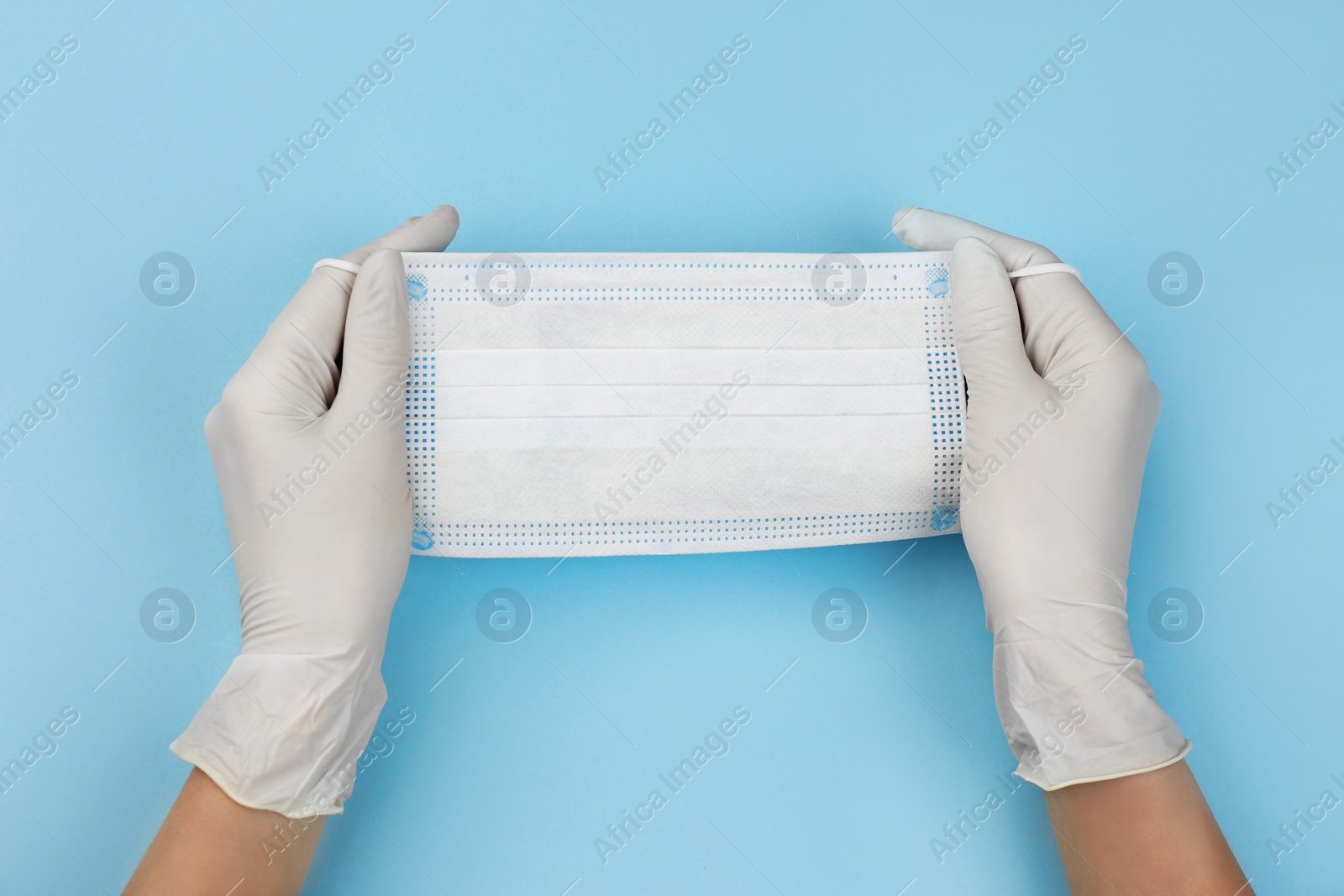 Photo of Doctor in medical gloves holding protective mask on light blue background, closeup