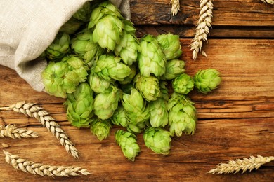 Sack with fresh green hops and wheat ears on wooden table, flat lay
