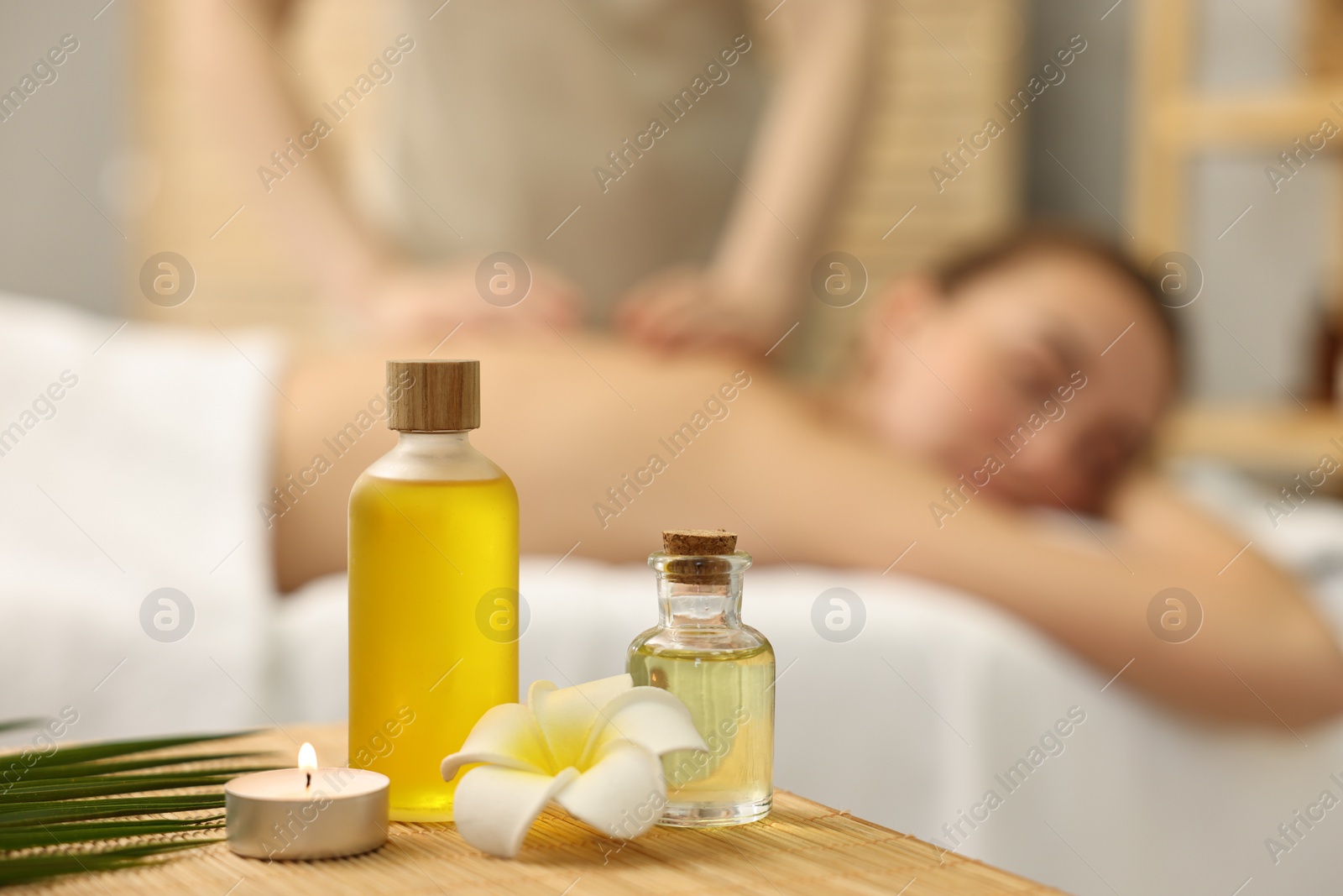 Photo of Aromatherapy. Woman receiving back massage in spa salon, focus on bottles of essential oils and burning candle