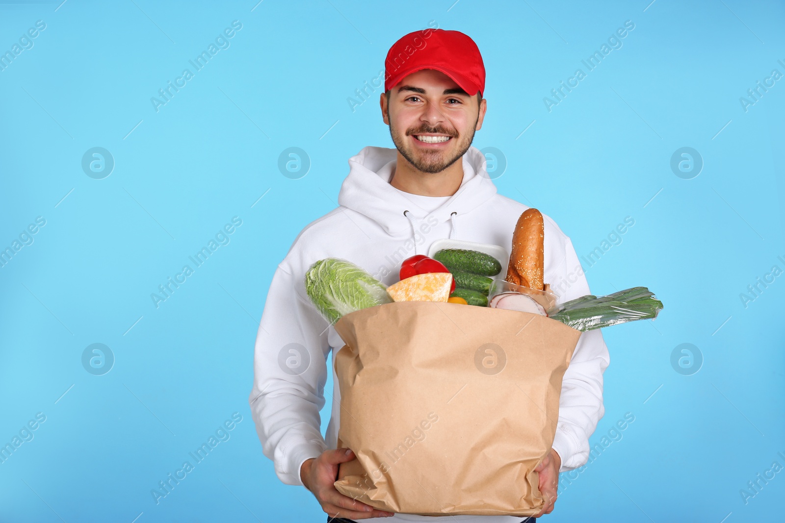 Photo of Young man holding paper bag with products on color background. Food delivery service