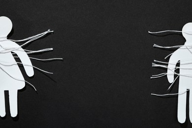 Photo of Divorce concept. Paper human figures with cut white threads on black background, flat lay. Space for text