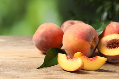 Photo of Cut and whole fresh ripe peaches on wooden table against blurred background, closeup