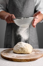 Photo of Man sprinkling flour over dough at table near grey wall, closeup