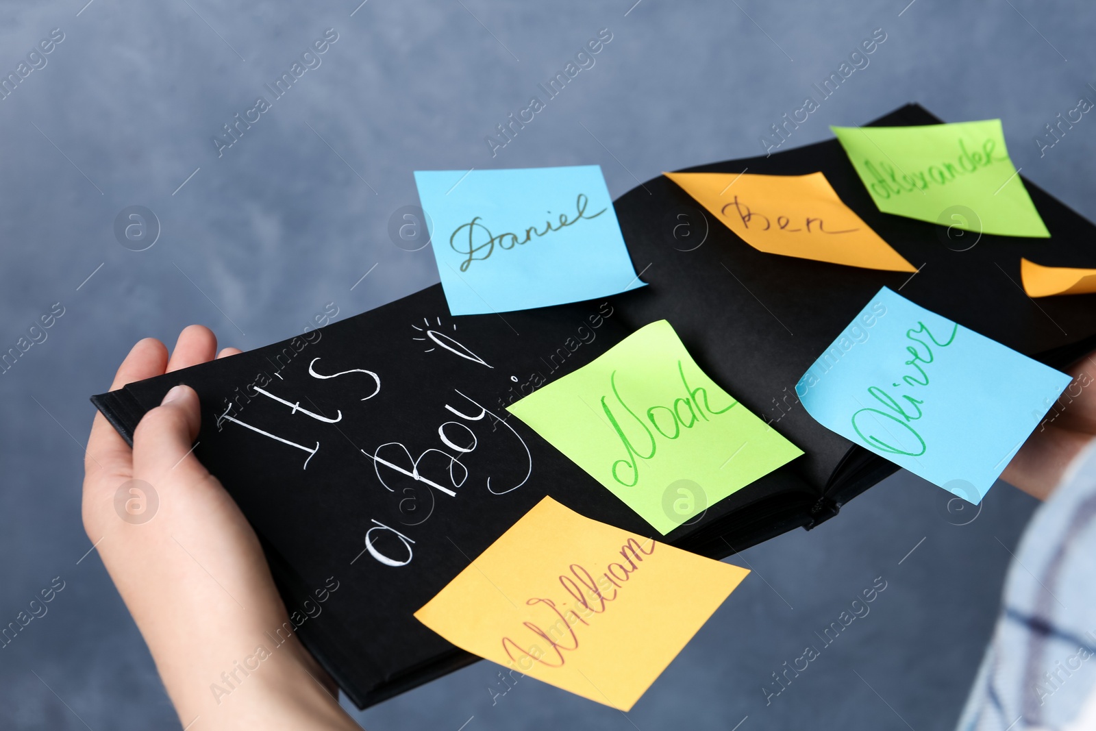 Photo of Woman holding notebook with written different baby names on grey background, closeup