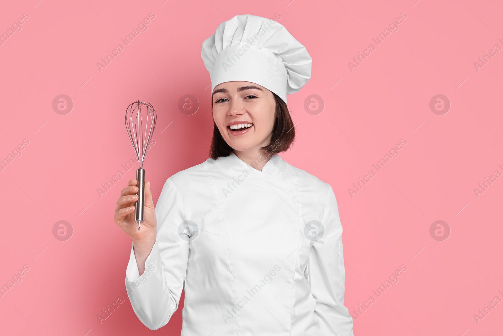 Photo of Happy confectioner with whisk on pink background