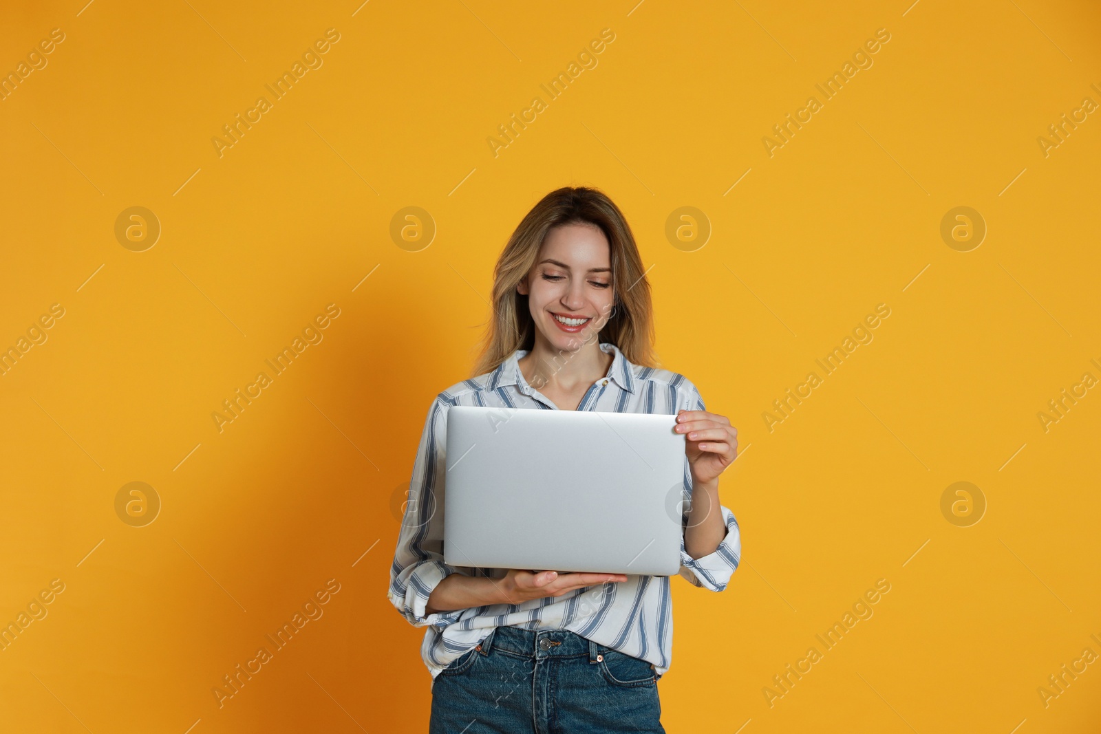 Photo of Young woman with modern laptop on yellow background