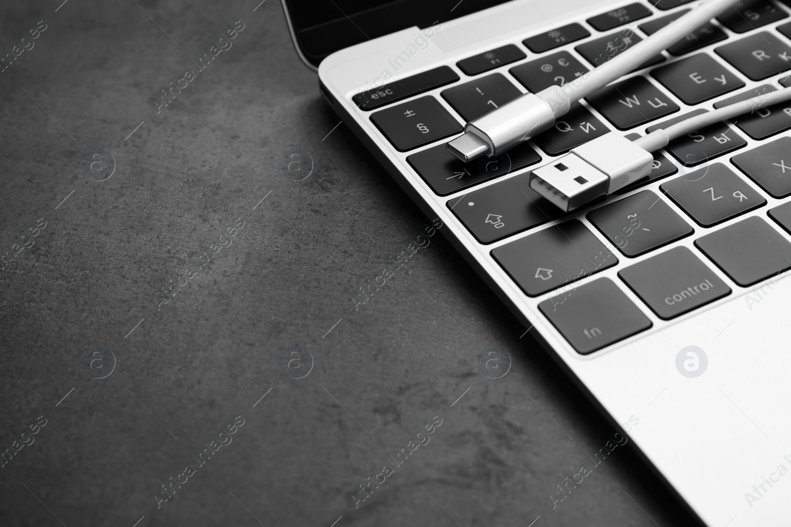 Photo of USB cable with type C connector and laptop on dark table, closeup. Space for text