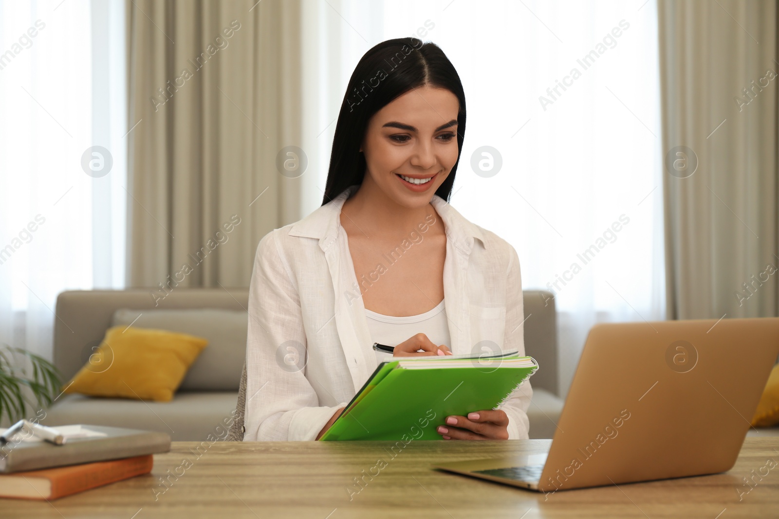 Photo of Young woman taking notes during online webinar at table indoors