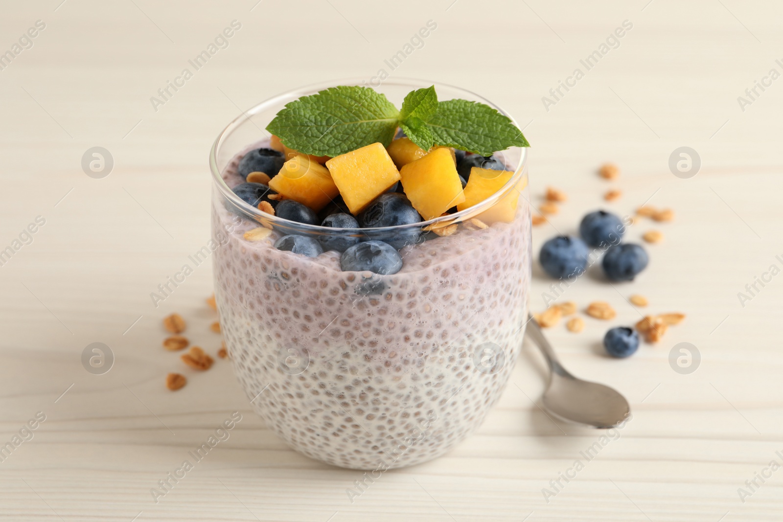 Photo of Delicious chia pudding with blueberries, mango and mint on white wooden table