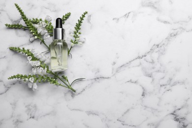 Bottle of essential oil and flowers on white marble table, flat lay. Space for text