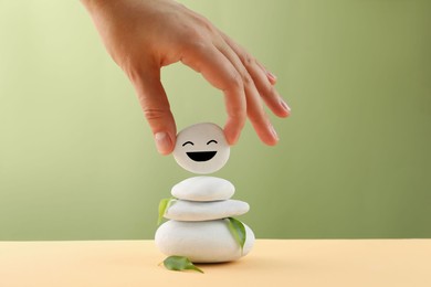 Photo of Woman putting stone with drawn happy face on stack, closeup Zen concept