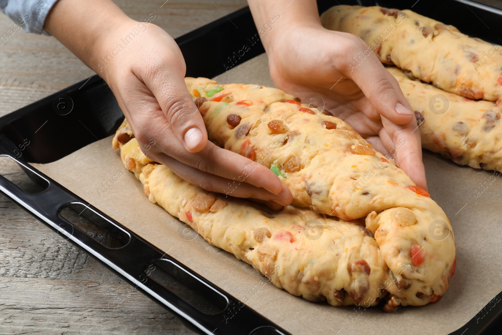 Photo of Woman making Stollen with candied fruits and nuts on baking tray at wooden table, closeup. Baking traditional German Christmas bread