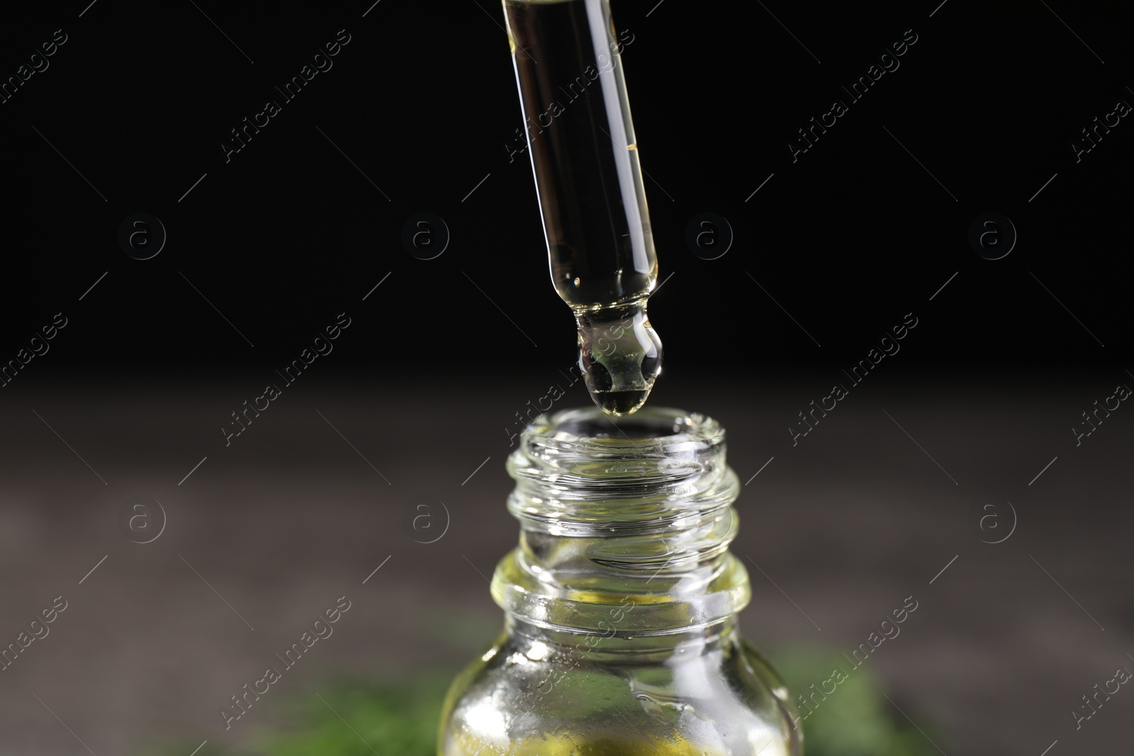 Photo of Dripping dill essential oil from pipette into bottle against black background, closeup