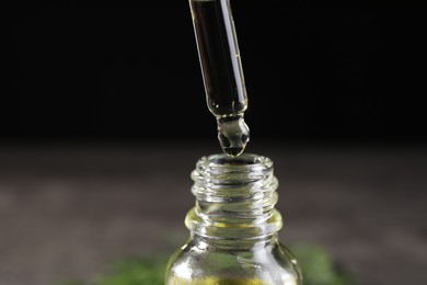 Dripping dill essential oil from pipette into bottle against black background, closeup