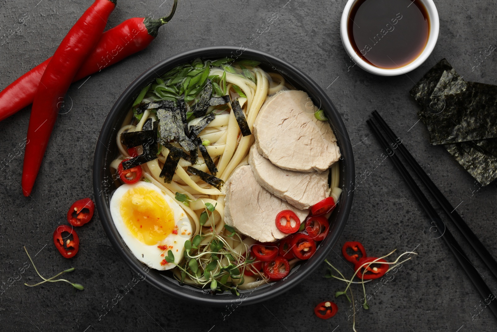 Photo of Delicious ramen with meat in bowl and ingredients on grey textured table, flat lay. Noodle soup