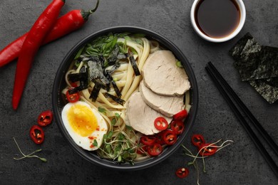 Photo of Delicious ramen with meat in bowl and ingredients on grey textured table, flat lay. Noodle soup