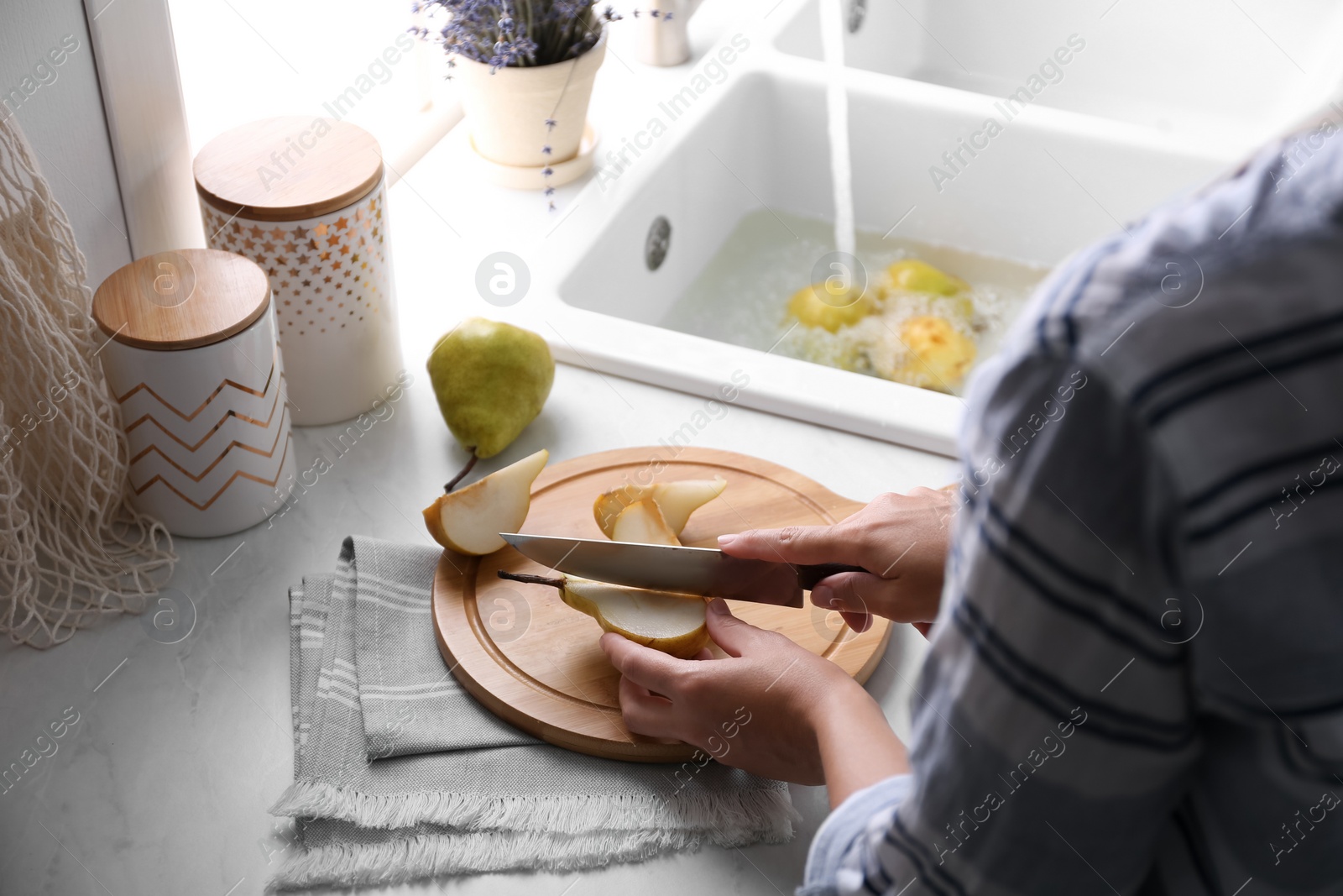 Photo of Woman cutting fresh ripe pear at table in kitchen, closeup