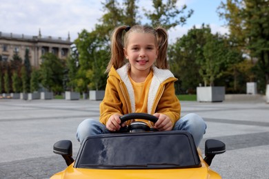 Cute little girl driving children's car on city street