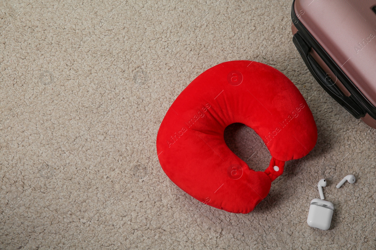 Photo of Red travel pillow, suitcase and earphones on beige rug, flat lay. Space for text