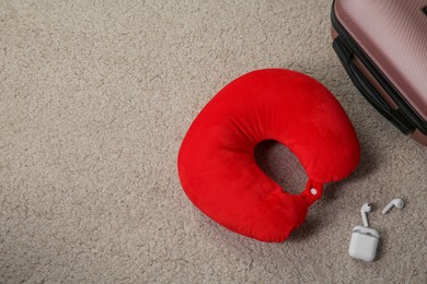 Photo of Red travel pillow, suitcase and earphones on beige rug, flat lay. Space for text