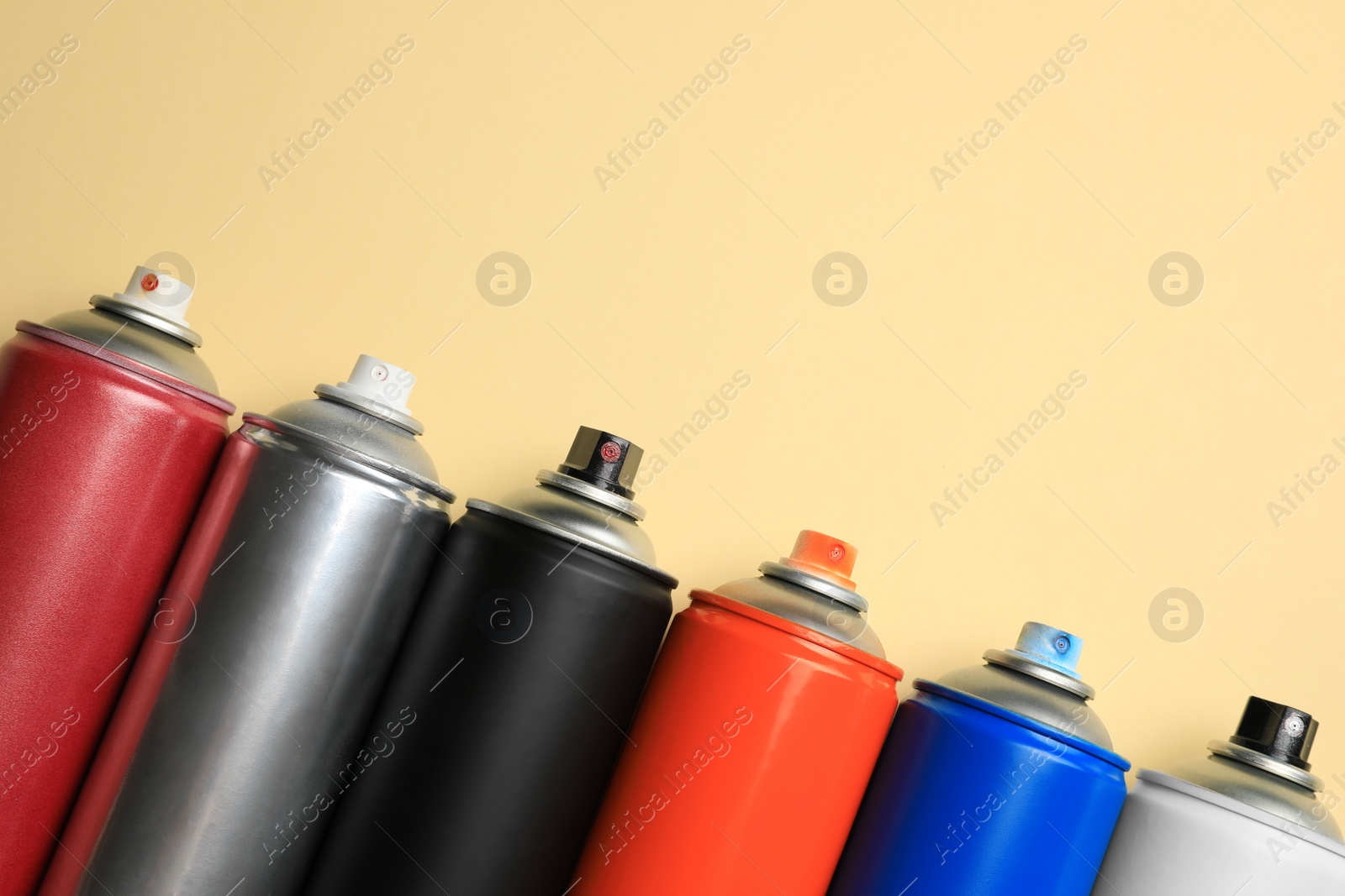 Photo of Cans of different spray paints on beige background, flat lay with space for text. Graffiti supplies