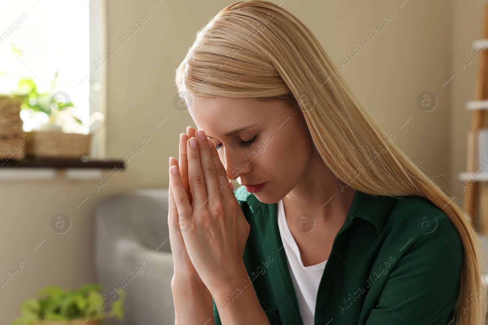 Photo of Religious young woman with clasped hands praying indoors