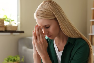 Photo of Religious young woman with clasped hands praying indoors