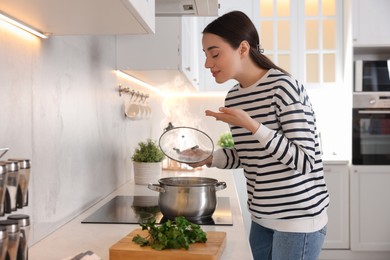 Photo of Beautiful woman smelling aromatic soup in kitchen
