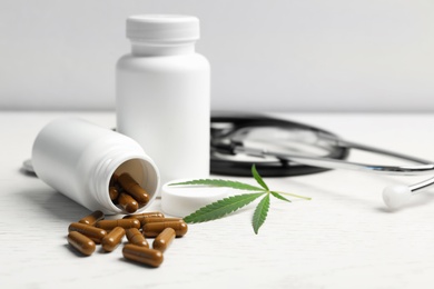 Photo of Hemp leaf, bottles with capsules and stethoscope on white wooden table