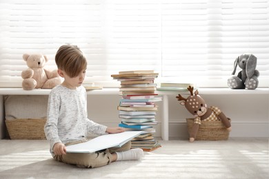 Photo of Little boy reading book on floor at home