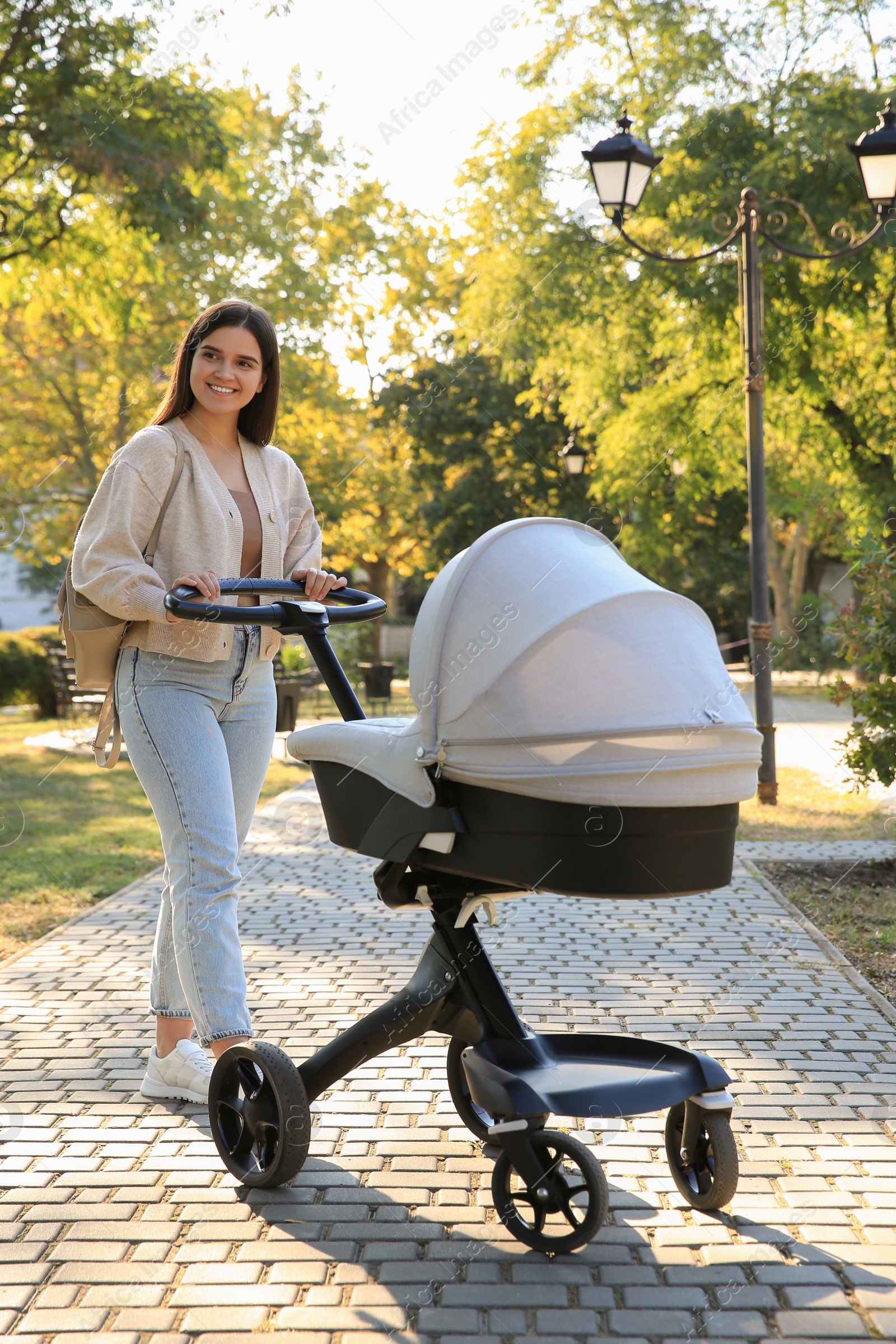 Photo of Young mother walking with her baby in stroller at park on sunny day