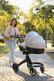 Young mother walking with her baby in stroller at park on sunny day