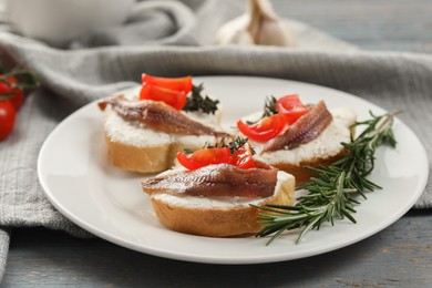 Photo of Delicious sandwiches with cream cheese, anchovies and tomatoes on grey wooden table