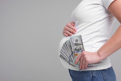 Photo of Surrogate mother. Pregnant woman with dollar banknotes on light grey background, closeup. Space for text