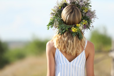 Photo of Young woman wearing wreath made of beautiful flowers outdoors on sunny day, back view