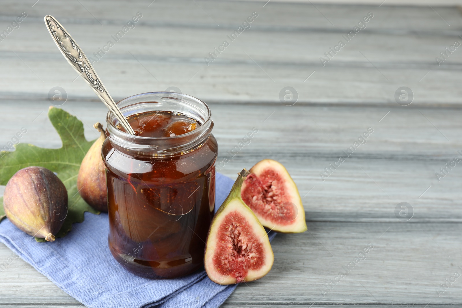 Photo of Jar of tasty sweet jam and fresh figs on grey table, space for text