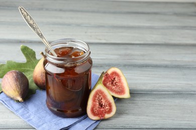 Jar of tasty sweet jam and fresh figs on grey table, space for text