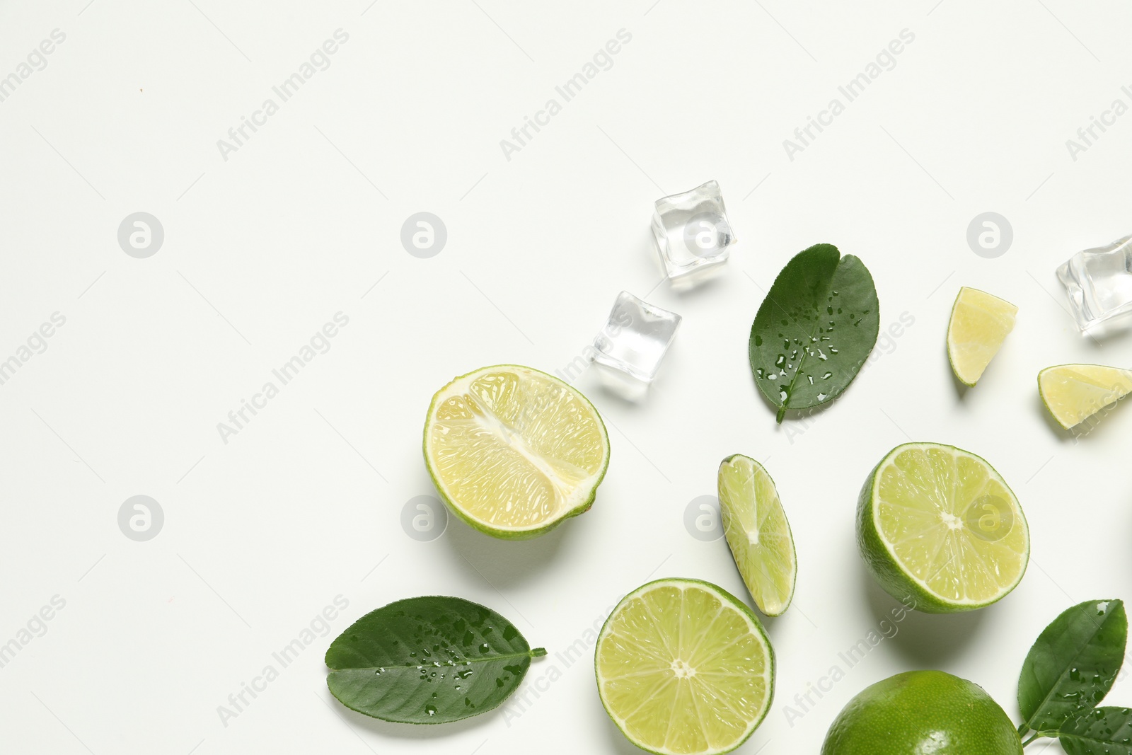 Photo of Fresh ripe limes with green leaves and ice cubes on white background, flat lay