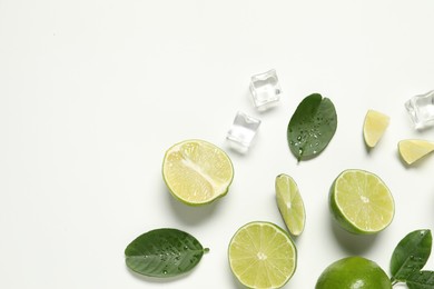 Fresh ripe limes with green leaves and ice cubes on white background, flat lay