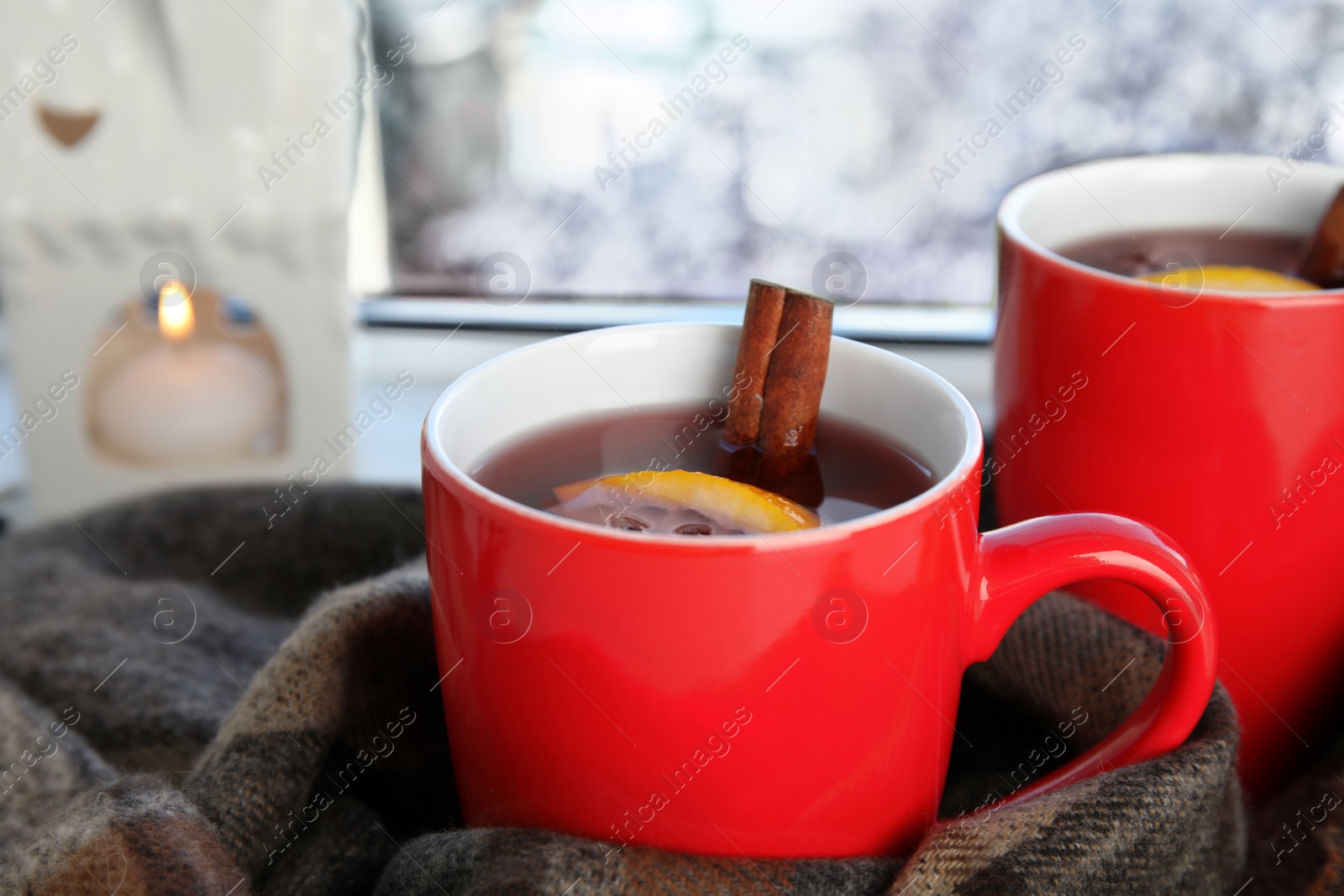 Photo of Cups of hot winter drink with scarf on window sill indoors, closeup