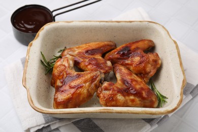 Photo of Fresh marinade, chicken wings and rosemary on white tiled table, closeup