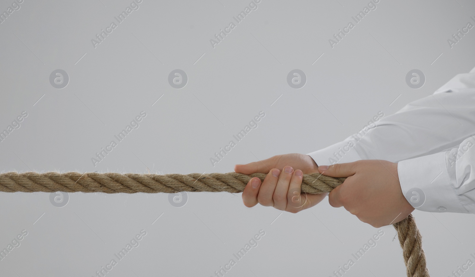 Photo of Dispute concept. Man pulling rope on light grey background, closeup