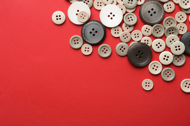 Many colorful sewing buttons on red background, flat lay. Space for text