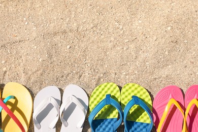 Photo of Many different flip flops on sand, flat lay. Space for text