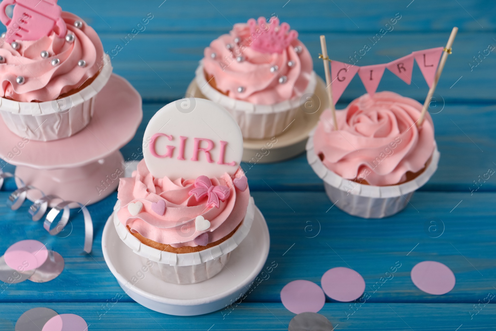 Photo of Delicious cupcakes with pink cream and toppers for baby shower on light blue wooden table