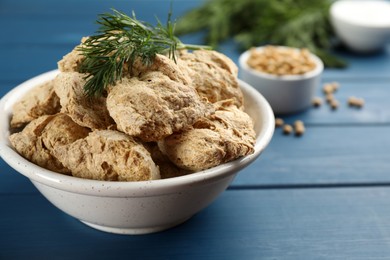 Photo of Dehydrated soy meat chunks with dill in bowl on blue wooden table, closeup