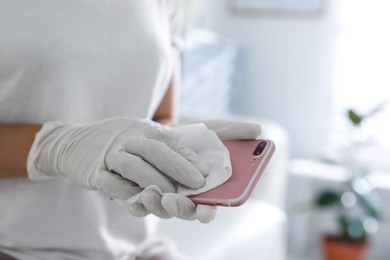 Photo of Woman cleaning mobile phone with wet wipe indoors, closeup