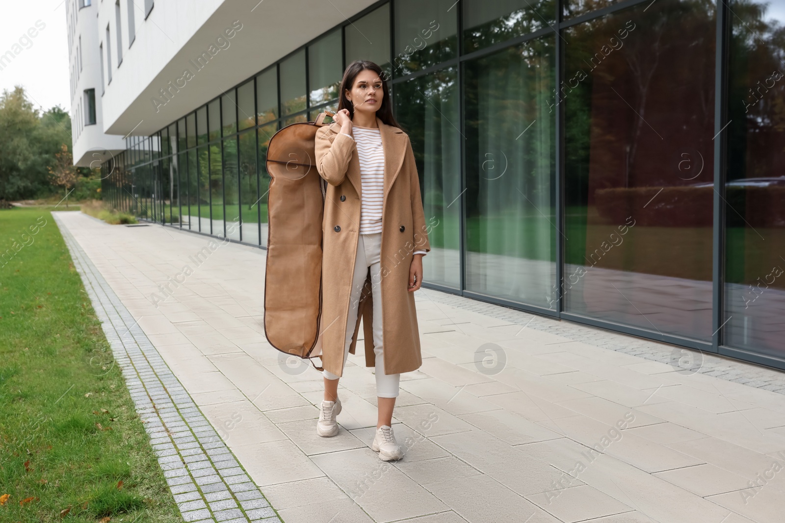 Photo of Attractive serious woman holding garment cover with clothes outdoors. Dry cleaning service